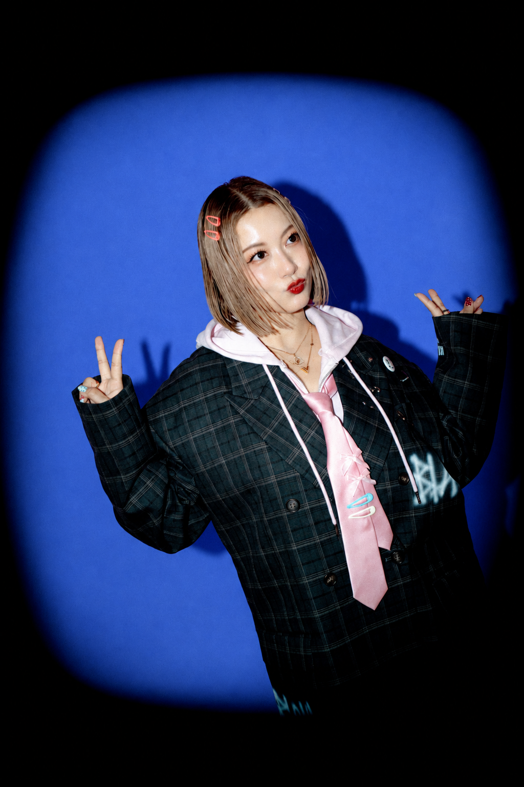 Nozomi Kitay making peace signs against a cobalt-blue background